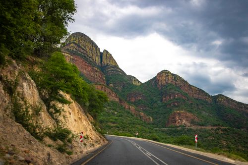 Free A scenic view of a winding highway passing through lush mountain terrain under a cloudy sky. Stock Photo