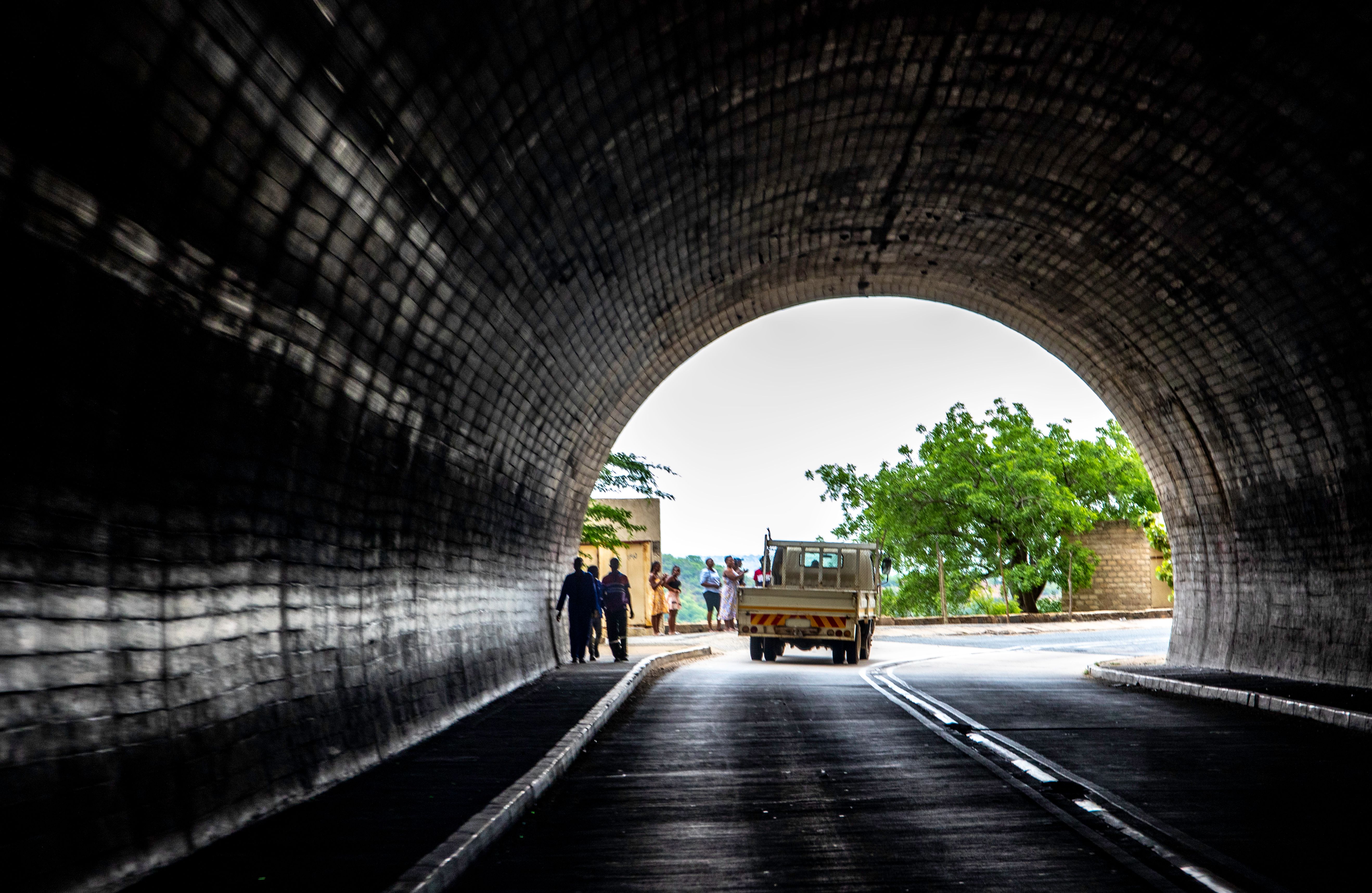 A rugged vehicle emerging from a dark urban tunnel into a sunlit street with people gathered nearby.