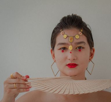 Portrait of a woman with traditional jewelry holding a folding fan.