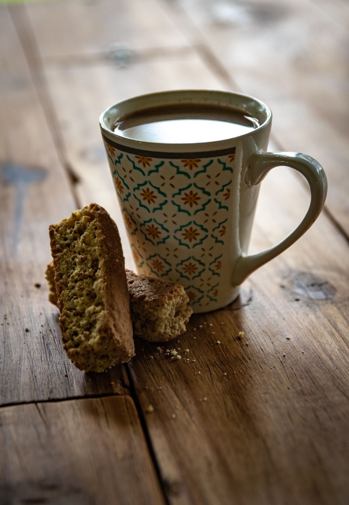 Almond biscotti beside a cup of coffee in a patterned mug on a rustic wooden table