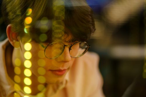 Free Portrait of a man wearing eyeglasses, surrounded by warm bokeh lights, conveying a thoughtful ambiance. Stock Photo