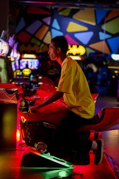 African American man playing arcade games in a colorful illuminated room, wearing a yellow shirt