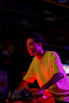 A young man enthusiastically plays a motorcycle arcade game with colorful lighting.