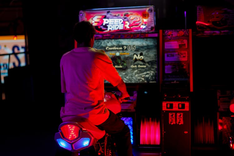 Back View Shot Of A Man Playing Motorcycle Arcade Game