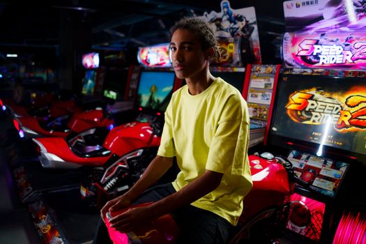 Teenage boy in arcade playing a motorcycle racing game with vibrant colors.