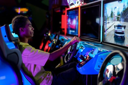 A young man intensely plays a car racing video game at an amusement arcade.