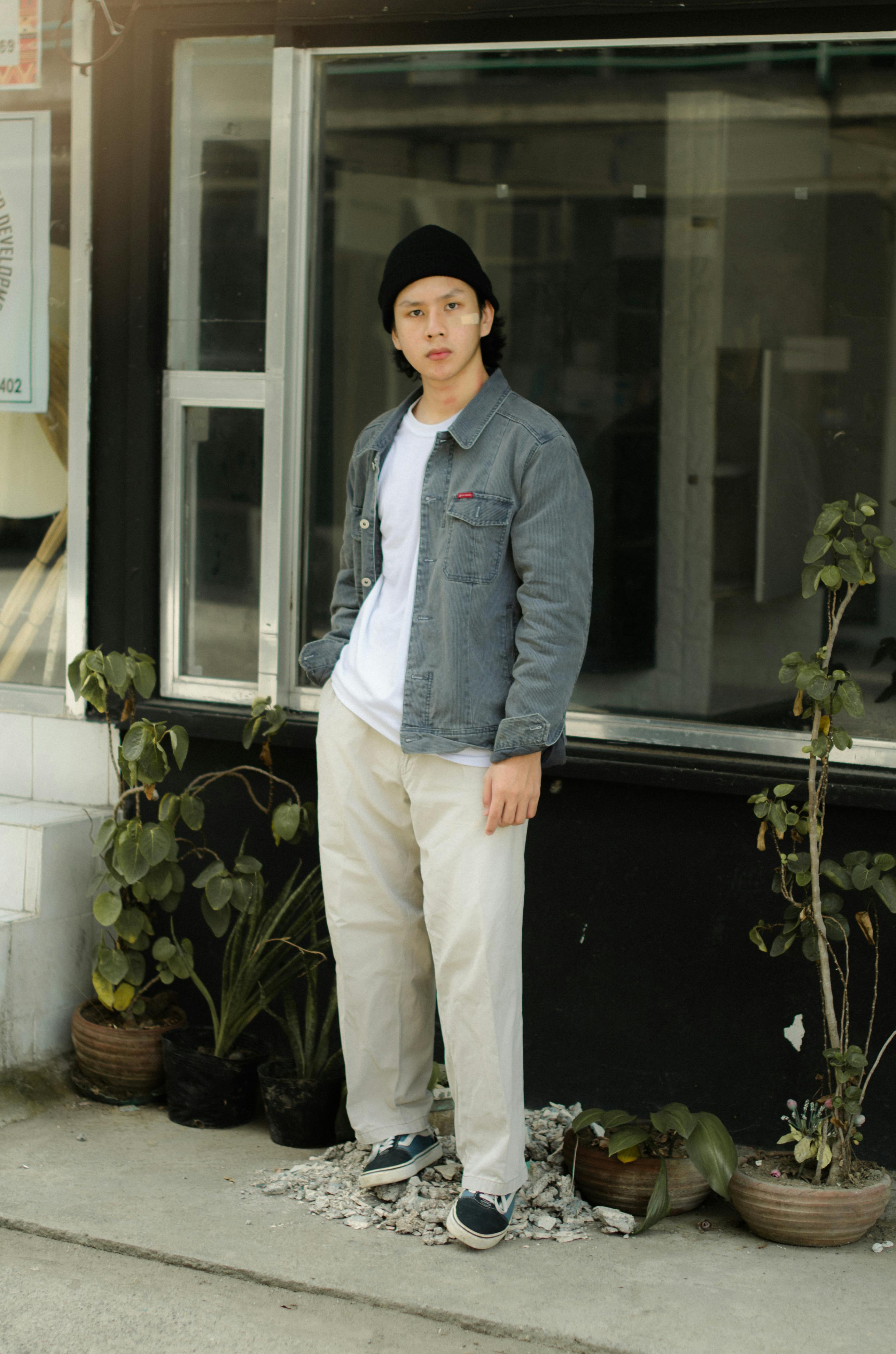Young Asian man in casual attire posing with potted plants.