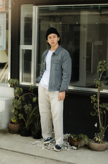 Young Asian man in casual attire posing with potted plants.