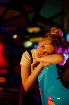 A blonde woman with a unique hairstyle rests on an arcade machine in a colorful gaming hall.