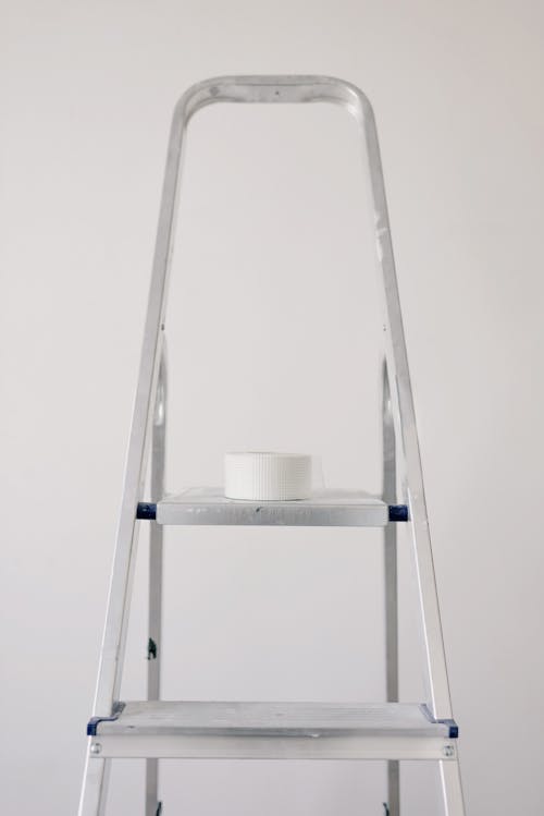 Metal ladder with roll of paper tape for renovation works in flat against white wall