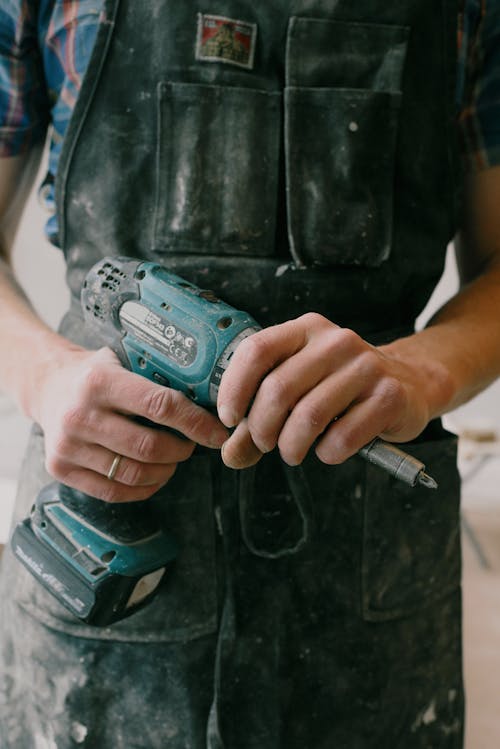 Free Crop anonymous mechanic in uniform with wireless drill standing in flat during repair works Stock Photo