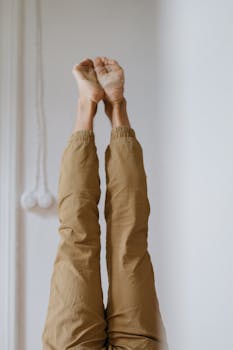 Vertical shot of a person performing an acro yoga pose with raised legs and bare feet indoors.