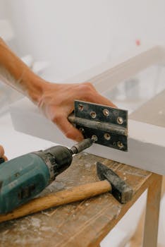 A handyman using a drill to install a hinge on a window frame indoors.