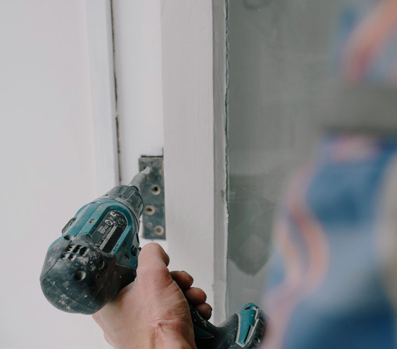Pose de fenêtre par un artisan Artisan installant une fenêtre en bois à la visseuse lors d'une rénovation