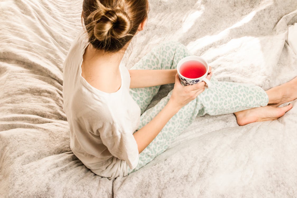 Aerial View Photography of Woman Sitting on Blanket While Holding Mug Filled With Pink Liquid Looking Sideward