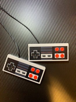 Two retro game controllers with a wired connection on a carbon fiber surface, top view.