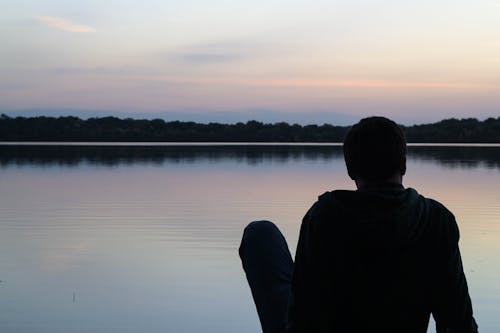 日落時分坐在前面大水域的男人穿運動衫的剪影攝影