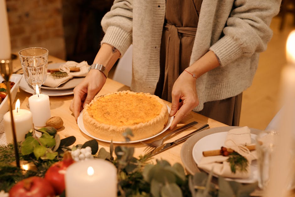 A person setting a pie on a beautifully decorated holiday dinner table with candles and winter greenery.