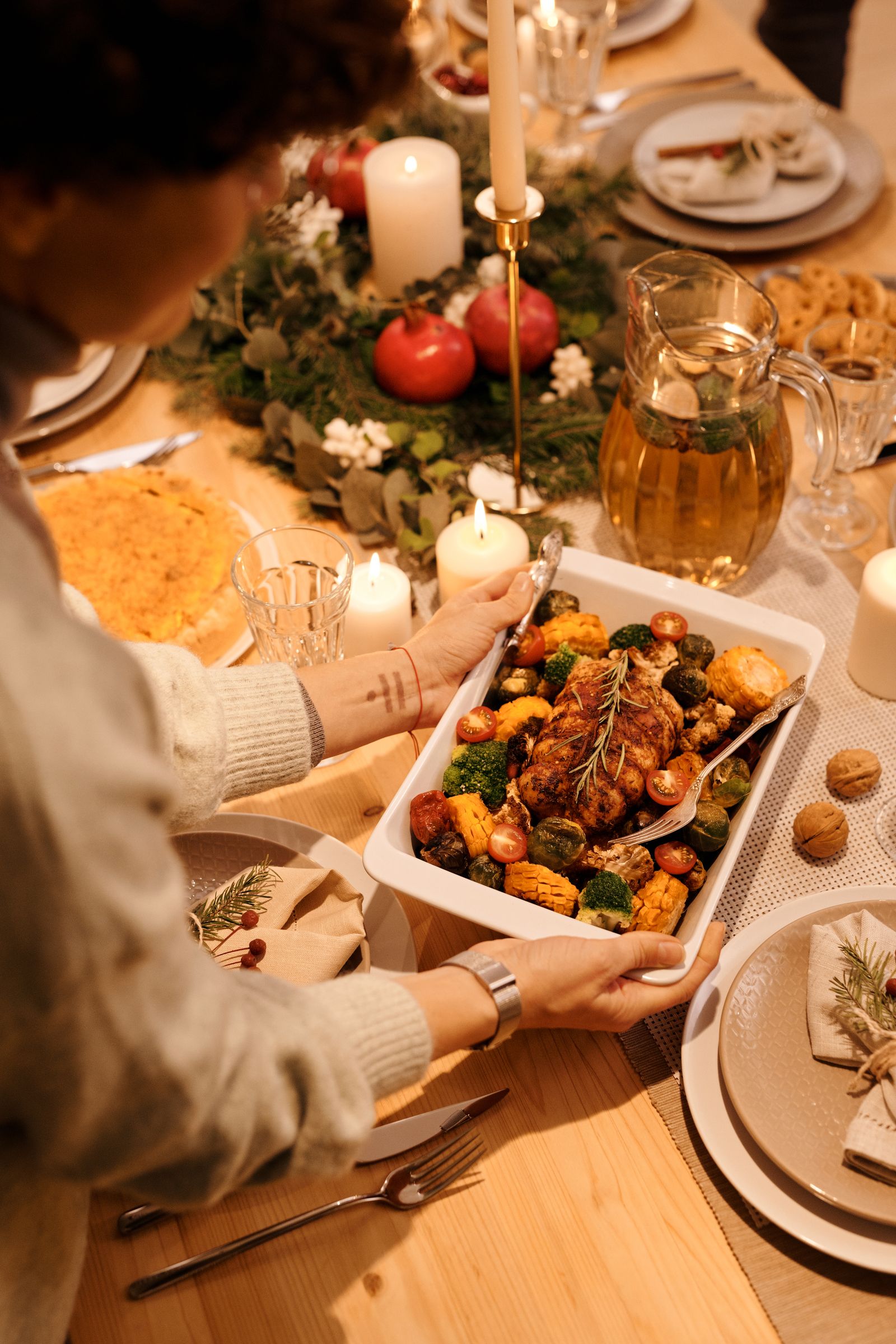Hands serving roasted vegetables at a festive Christmas dinner table.