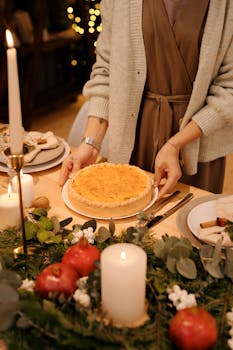 A person sets a quiche on a decorated holiday table with candles and festive decor.