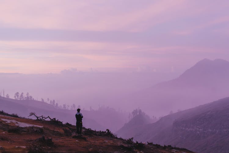 Silhouette Of Person Standing On A Cliff Of A Mountain