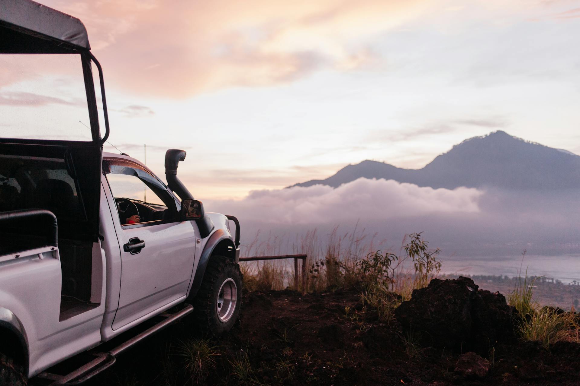 A pickup truck parked on a cliffside with scenic mountain views at sunrise.