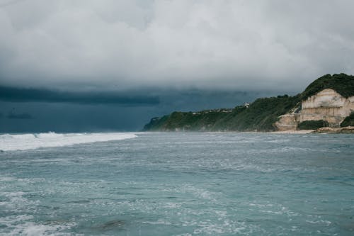 白い雲の下の水域の横にある緑の山