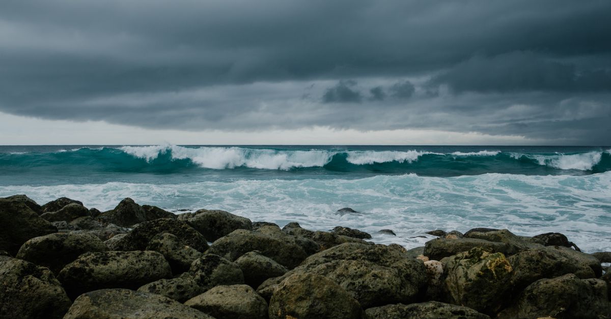 Photo by Julia Volk Powerful ocean waves crashing against rocks under a dark, stormy sky.