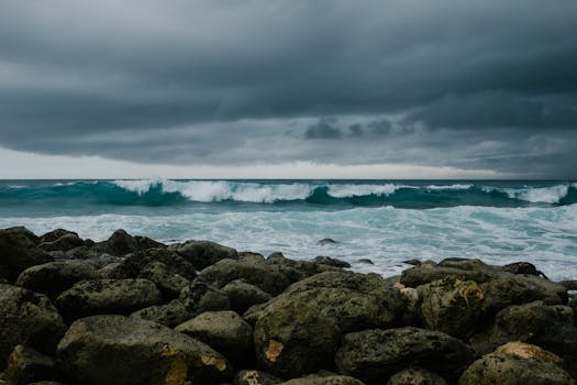 Powerful ocean waves crashing against rocks under a dark, stormy sky.