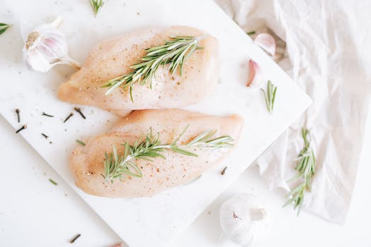Raw chicken breasts seasoned with rosemary and garlic on a cutting board.