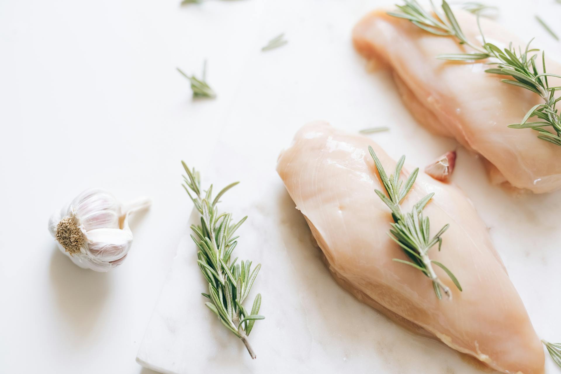 Fresh Raw Chicken Meat with Rosemary Toppings on White Surface