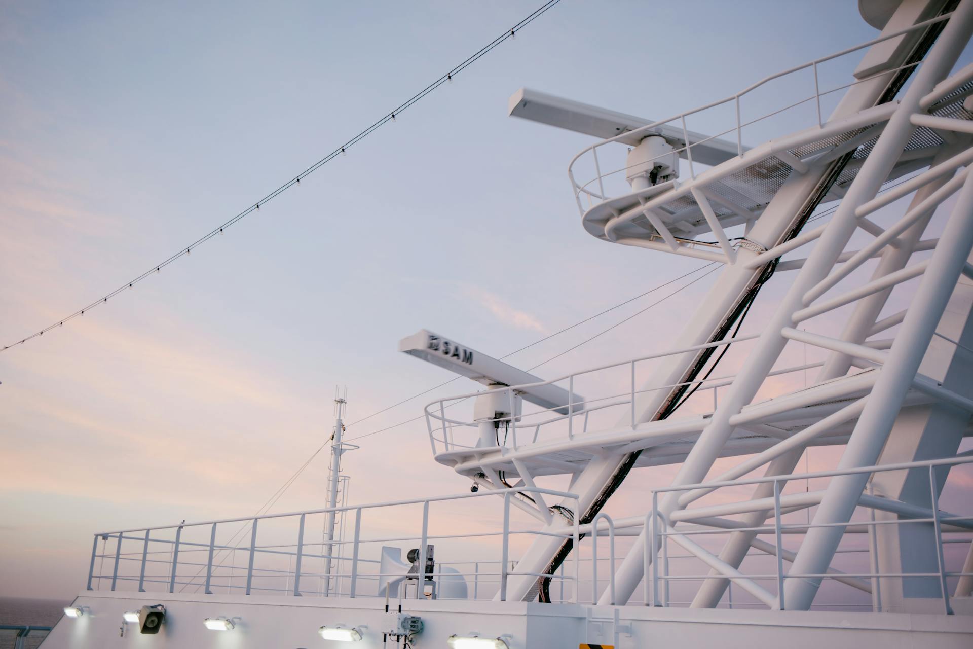 Close-up of a modern ship's radar tower and telecommunications equipment against a pastel sunset sky.