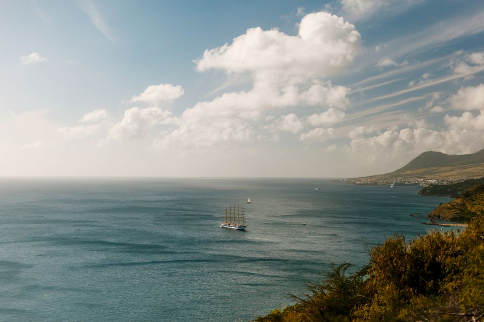 A serene landscape with a sailing ship on the vast ocean and a picturesque coastline.