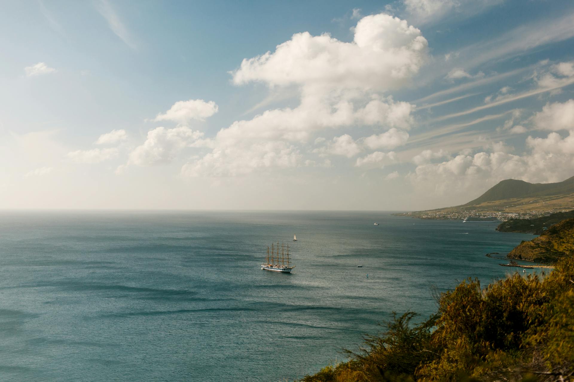 A serene landscape with a sailing ship on the vast ocean and a picturesque coastline.