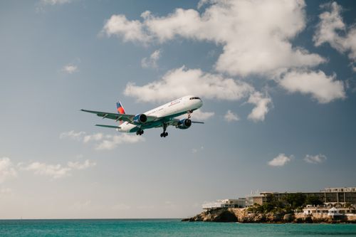 Free Commercial aircraft landing above ocean with clear blue skies, near beach resort. Stock Photo