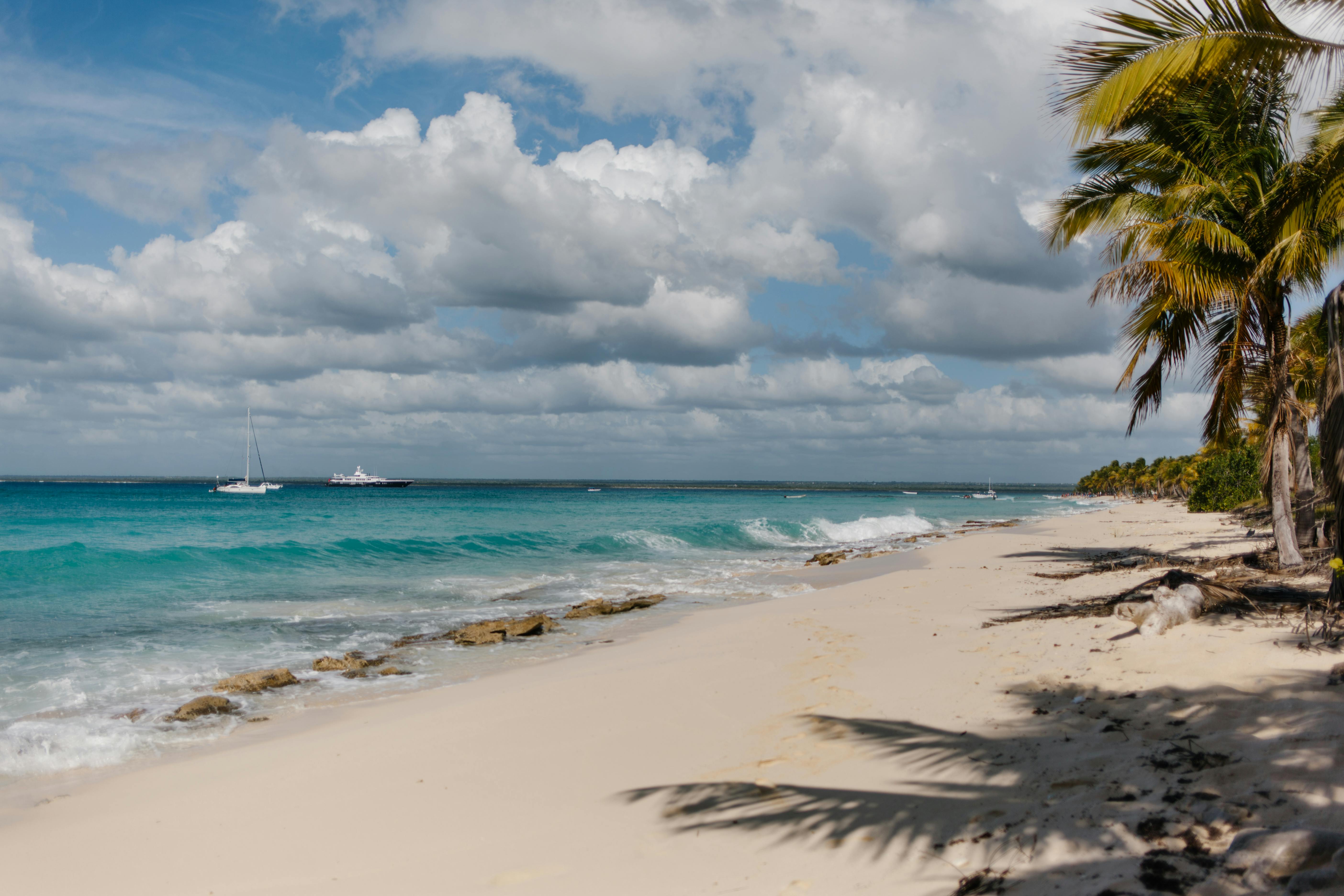 宁静的热带海滩，棕榈树，白色沙滩和多云的天空下碧绿的海面上的船只