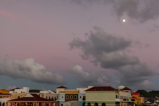 Colorful urban cityscape at dusk with a dramatic cloudy sky and moon overhead.