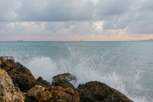 Costa Rochosa Marrom Com Ondas Do Mar Sob Nuvens Brancas