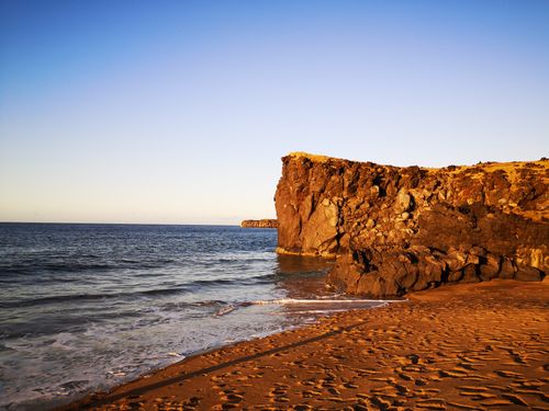 Free Dramatic cliff at sunset on a sandy Icelandic beach with ocean waves. Stock Photo