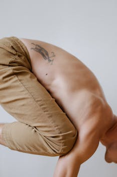 A man performs a shirtless acro yoga pose, showcasing balance and a prominent tattoo.