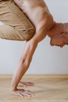 A man performs an advanced yoga pose indoors, showcasing balance and strength.