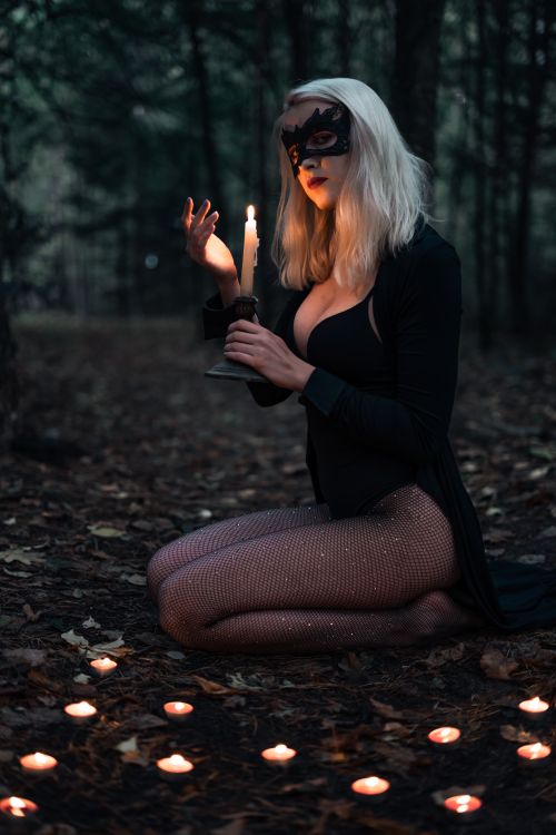 Free Side view of young seductive blond female in decorative mask sitting on land near burning candles while looking at camera at night Stock Photo
