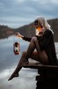 Side view of young barefoot female in carnival mask touching hair on dock near river while looking forward in evening