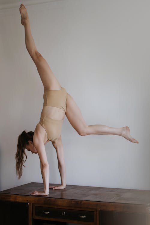 Woman in Beige Active Wear Doing Handstand on a Wooden Table