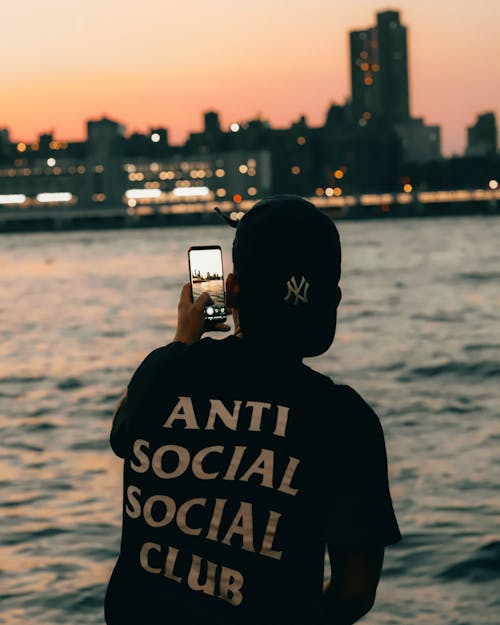 Man in Black Shirt Taking Photos of the Sea Using a Cellphone