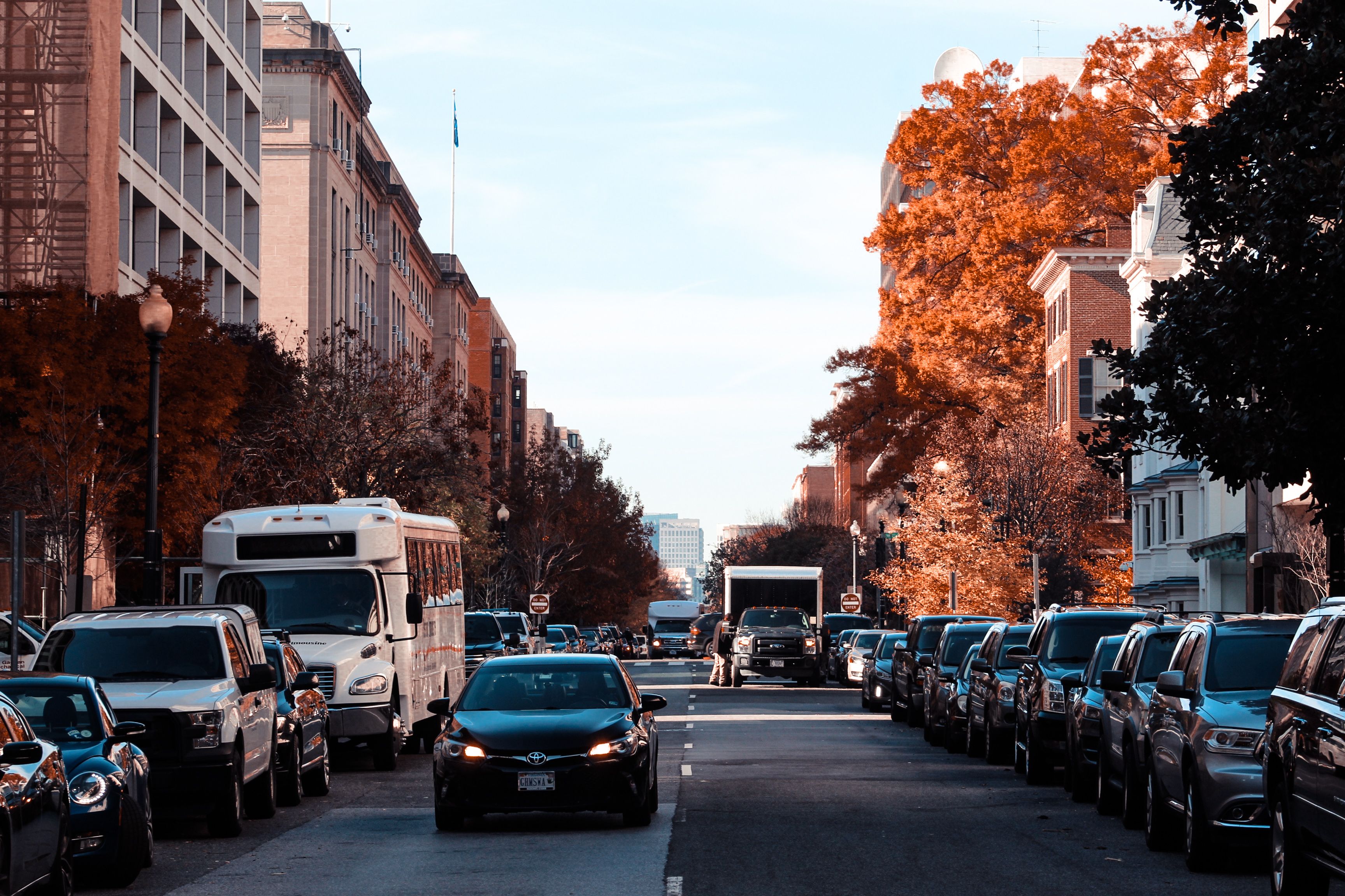 A city street lined with autumn trees, cars, and urban buildings on a sunny day.