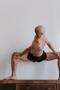 在简约的背景下，一名光着膀子的男人在室内做瑜伽，展示出灵活性与平衡性