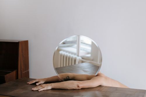 Free Artistic shot of arms holding a round mirror, reflecting a minimalist interior with wooden furnishings. Stock Photo