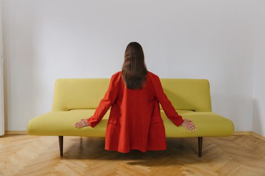 一个穿着红色夹克的女人背对着坐在木地板上的现代黄色沙发上