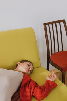 一位身着红色西装外套的女人镇定地躺在时尚的石灰绿色沙发上